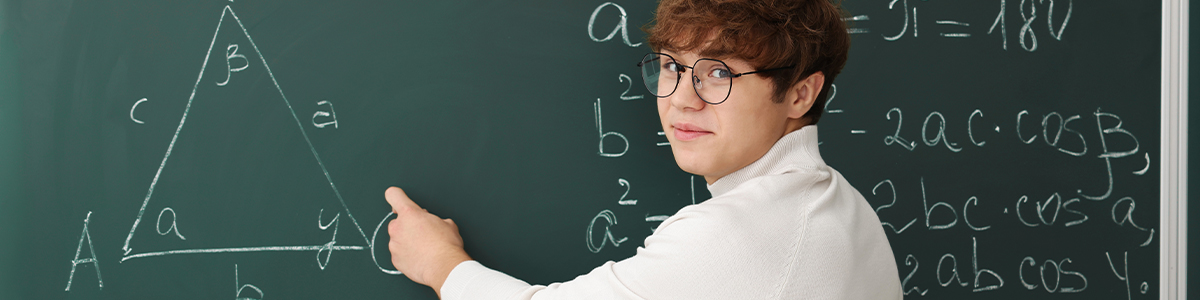 A young man with glasses points at a chalkboard covered with math formulas and a triangle diagram.