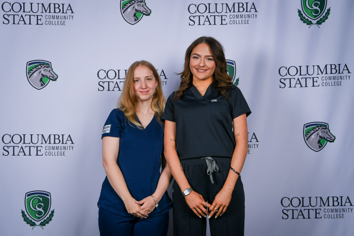 Two women pose in front of a white background.