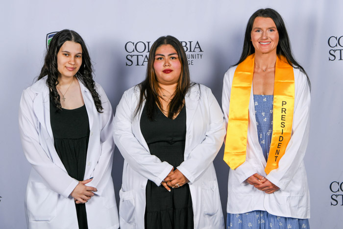 Three people stand in front of a white background.