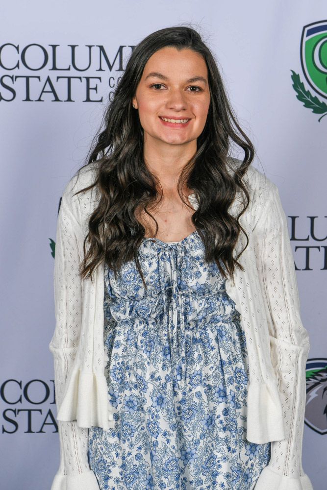 A woman stands in front of a white background.