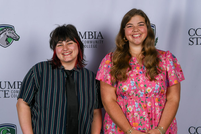 Two women stand in front of a white background.