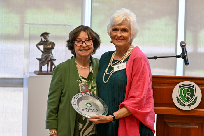 Two people smile for a photo. The person on the right hold a plate-shaped award.