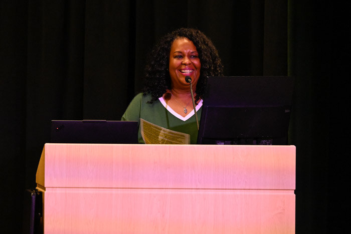 A person wearing a green shirt speaks from behind a lecture on a stage.