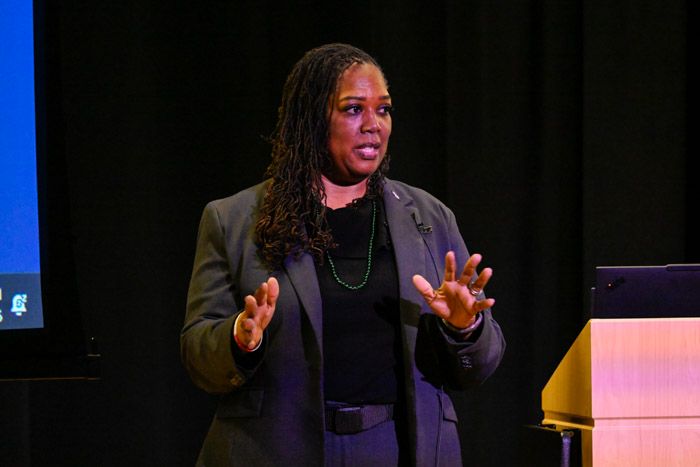 A person in a gray suit speaks on stage.