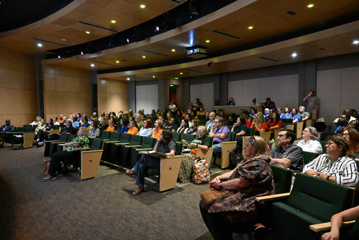 A photos shows a room full of people sitting in a theater.
